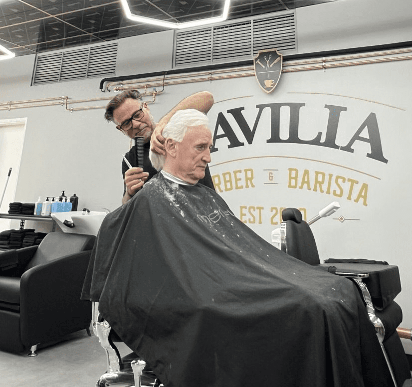 A barber cutting a senior man's hair in a well-lit salon